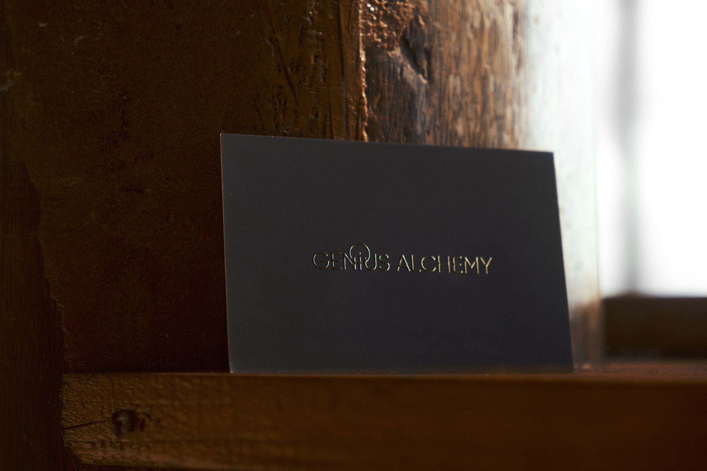 Front of the Genius Community business card, showing the logo on a sleek black background with gold embossed writting.
